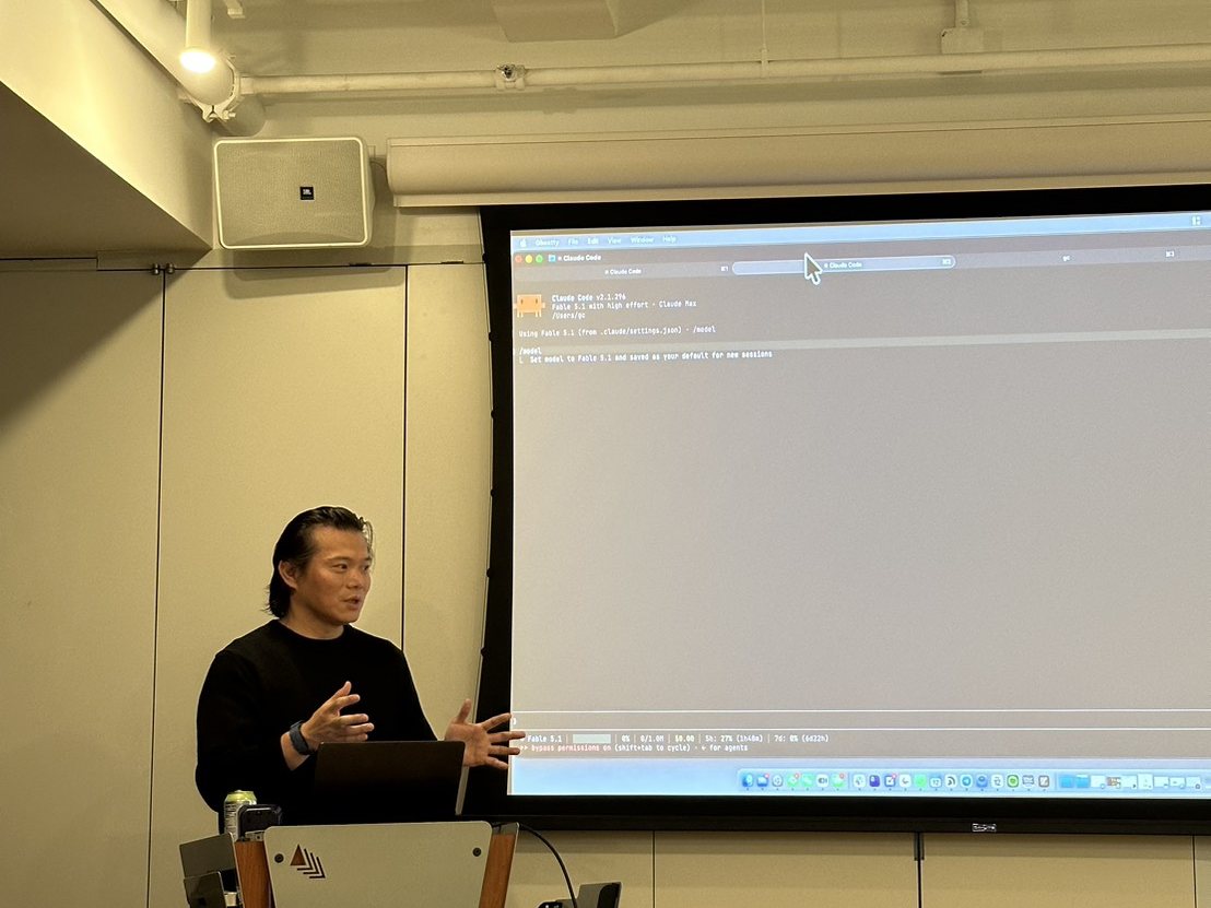 Gordon talking next to the projector, which shows Claude Code running in a Ghostty terminal