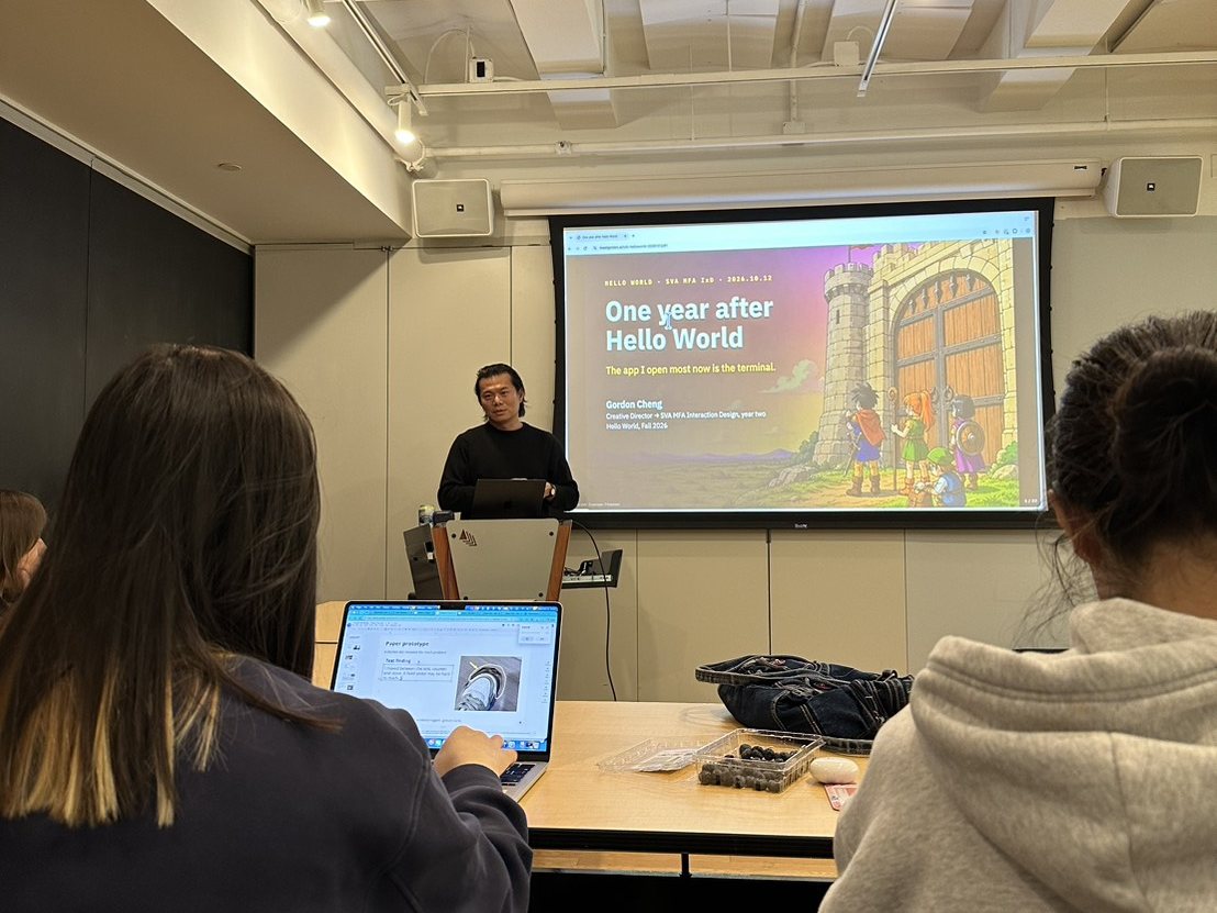 Gordon at the podium in the Hello World classroom, the cover slide One year after Hello World on the screen behind him